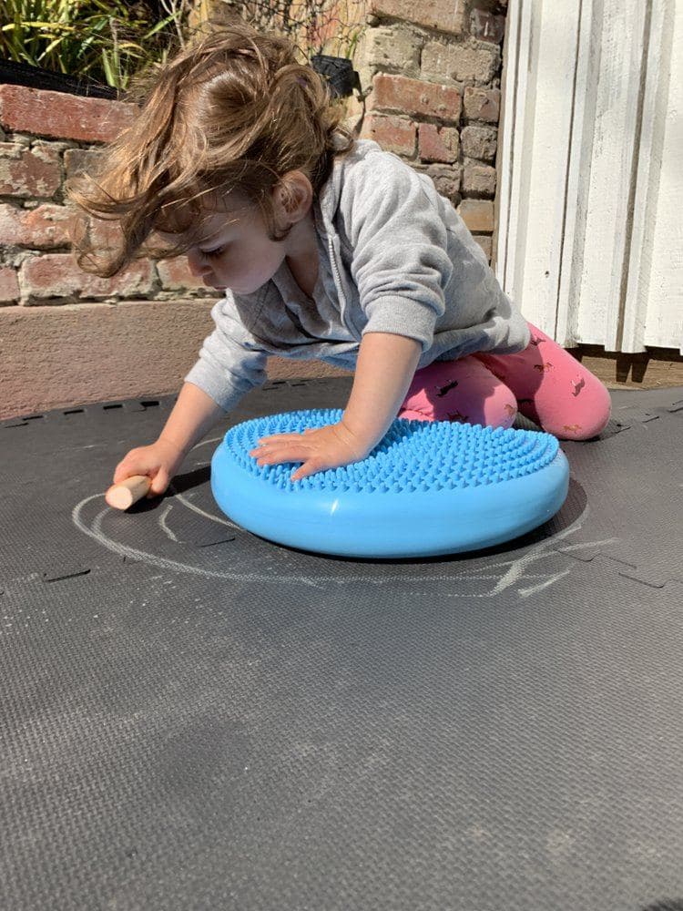 A young child explores a textured balance disc during hands-on outdoor play at Wisely SF